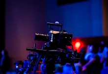 A professional broadcast camera filming a live studio event with an audience in the background.