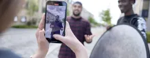 A creator is filmed in vertical video on a smartphone held in portrait orientation outdoors.