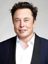 A portrait photograph of Elon Musk in a dark jacket and white shirt against a light background.