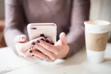 A woman holding an iPhone in both hands at a table.