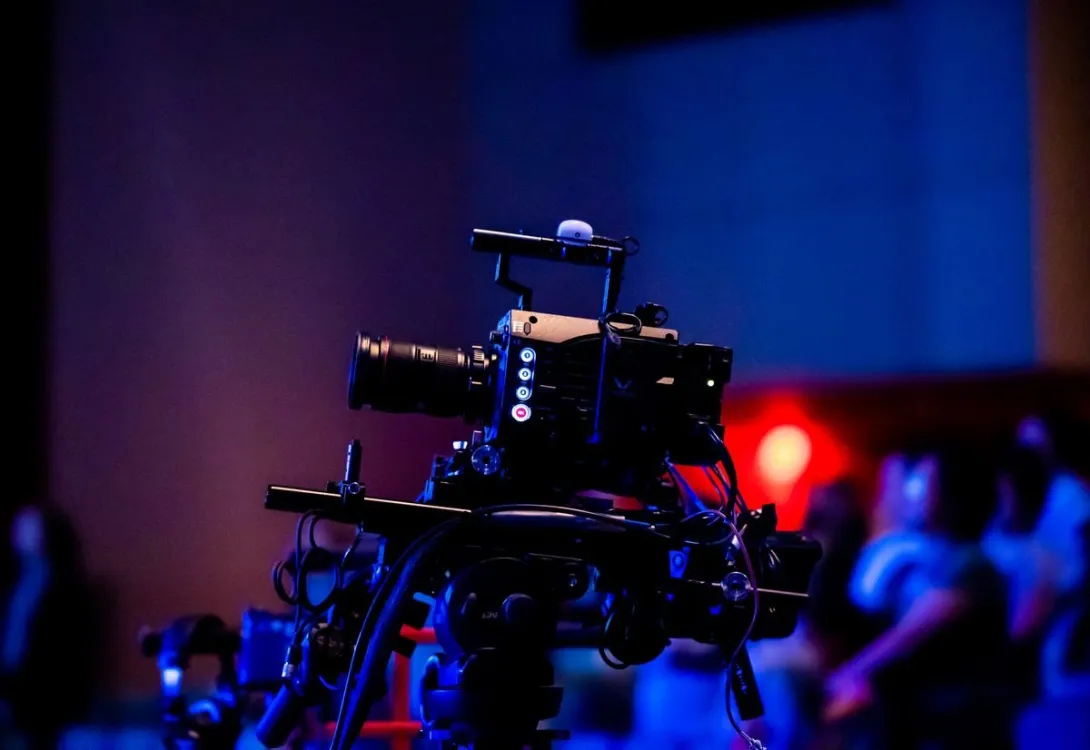A professional broadcast camera filming a live studio event with an audience in the background.